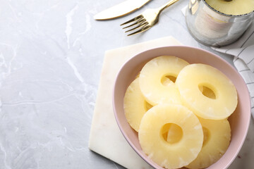 Delicious canned pineapple in bowl on light grey marble table, above view. Space for text