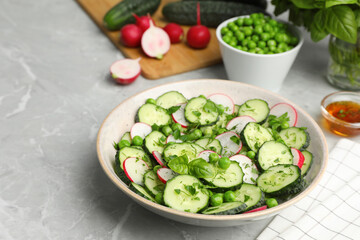 Appetizing salad with cucumbers, radish and pea in bowl on light grey table