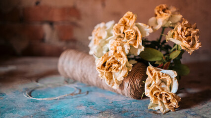 On the table there is a bouquet of white fading roses, a large skein of beige threads, scattered puzzles - against the background of a plastered brick vintage wall