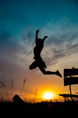 The silhouette of a child in a jump against the background of a beautiful sunset sky and a yellow sun