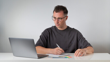 A guy at a laptop makes notes in a notebook at the workplace - work and study