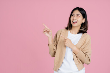 Smiling young asian woman standing pointing index fingers aside up on mock up copy space isolated on pink background. Mock up copy space. Pointing index fingers aside up.