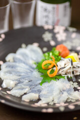 繊細に引かれた透き通るような身を、桜が舞う美しい器に並べた贅沢なとらふぐのてっさ。素材のしっとりとした質感が際立つ一皿で、高級和食店の冬メニューや特別な宴会、地酒を楽しむ席の販促に最適な高品質素材です。   Exquisite fugu sashimi, thinly sliced pufferfish on a cherry blossom plate. © Photo Craft