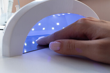 Female hand inside drying UV light machine in nail salon.