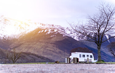 Caravan/motorhome against a wild backdrop of snow-capped mountains, with atmospheric glow effect 