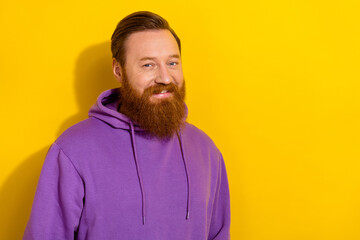 Portrait of positive young guy in comfy violet hoodie have long ginger beard isolated on yellow...