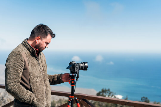 young photographer standing on lookout point taking pictures to the landscape over pacific ocean 