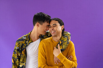 Happy biracial couple embracing with eyes closed and smiling on purple background