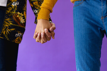Mid section of biracial male couple holding hands on purple background - Powered by Adobe