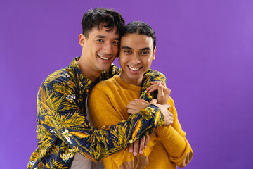 Portrait of happy biracial couple embracing and smiling on purple background