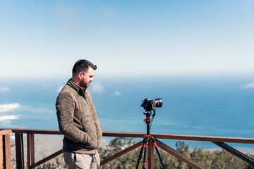 Obraz premium young photographer standing on lookout point making time lapses to the landscape over pacific ocean .