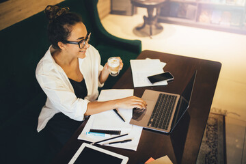 Young woman student drinking coffee and studying in library using laptop, smartphone and notebook.