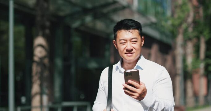 Man office worker, browsing smartphone during a walk on a sunny city street