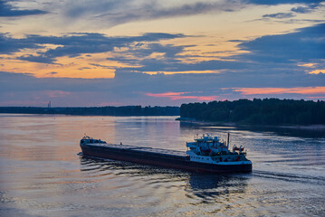 A barge floats on the river at sunset.