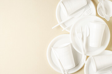 Disposable white plastic tableware on a beige background. The concept of nature pollution. Copy...