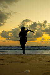 A girl running on the beach over the sands, orange horizon with clouds, waves, black shadow object