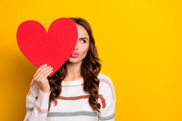 Photo of adorable lady arm hold heart symbol card cover eye pouted lips look empty space isolated on yellow color background