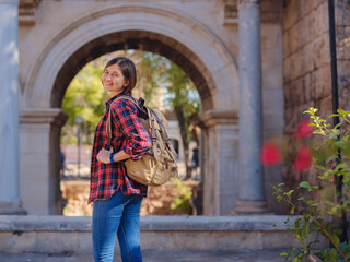 Fototapeta na wymiar travel to Turkey. Happy asian female tourist traveller with backpack walks in old city. Woman against backdrop of Hadrian's gate - popular attraction in old city of Antalya