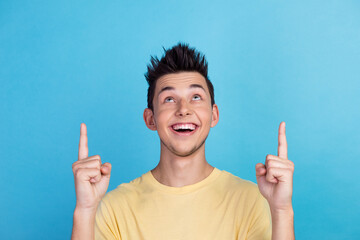 Portrait of amazed happy young man pointing fingers up at copy space isolated over blue background