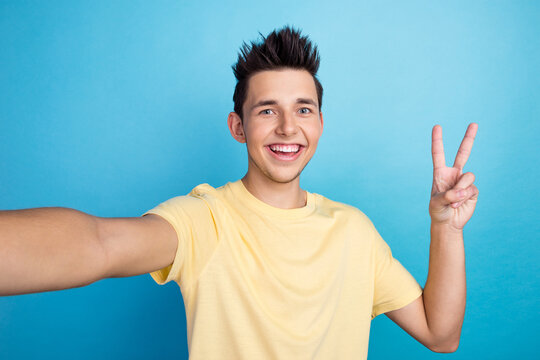 Beautiful excited young man makes self portrait v sign smiling isolated on blue color background