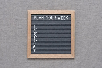 Plan your week text on letter board. Gray felt board on a gray textile background. Top view, flat lay. Day of the week with copy space.