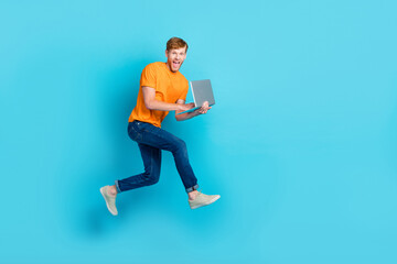 Full size profile photo of hooray red hair guy run with laptop wear t-shirt jeans boots isolated on blue color background