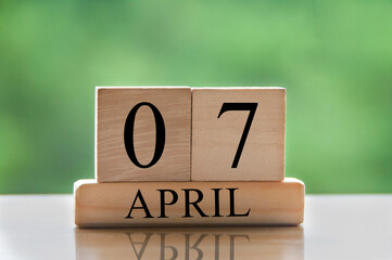 April 7 calendar date text on wooden blocks with blurred park background. Copy space and calendar...