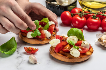 Woman hands preparing caprese bruschetta in the kitchen. Delicious breakfast or snack, Clean eating, dieting, vegan food concept. top view