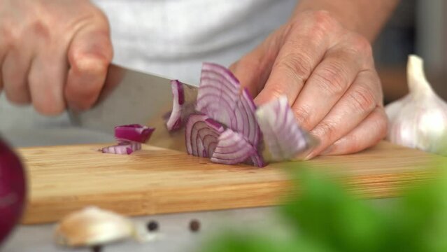 Camera movement on hands chop fresh red onion on wooden cutting board on background of vegetables and greens. Cooking food