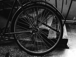 An old vintage bicycle stands next to the stairs indoors, the rear wheel is photographed, a concrete staircase is also visible, a vintage still life