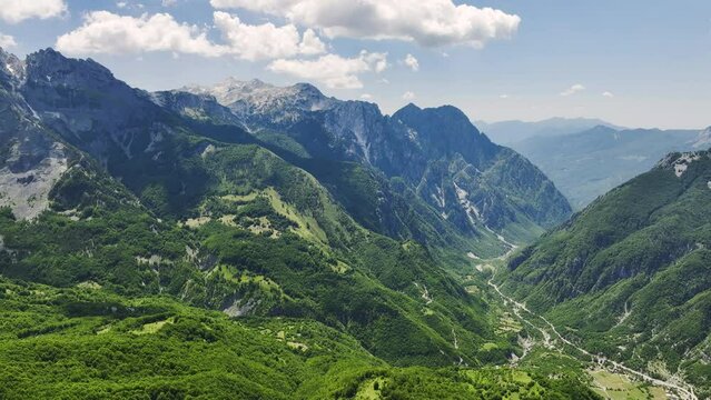 Aerial view of the Valbona river valley, green valleys, blue sky with clouds, steep rocks, remnants of snow. Hikers paradise. Theth national park, june, Albanian Alps, Albania.