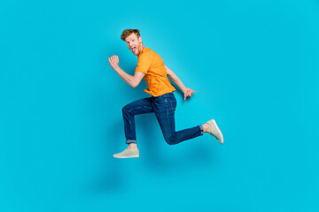 Fototapeta na wymiar Full body photo of cool red hair guy run wear t-shirt jeans boots isolated on blue color background