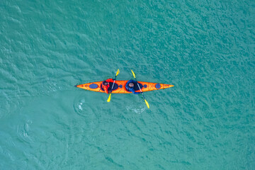Red kayak boat two rowers on blue turquoise water sea, sunny day. Concept teamwork for business plan, aerial top view - obrazy, fototapety, plakaty