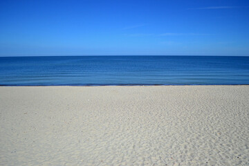 Beach on the Curonian Spit (Kurshskaya Kosa). Almost white sand. Blue calm Baltic Sea. In the photo at three standing only sand, sea, sky. Idyll. Symmetrical horizontal photo, Kaliningrad region
