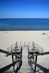 Beach on the Curonian Spit (Kurshskaya Kosa). Almost white sand. Blue calm Baltic Sea. In the foreground is a wooden staircase descending to the beach. Symmetrical vertical photo, Kaliningrad region