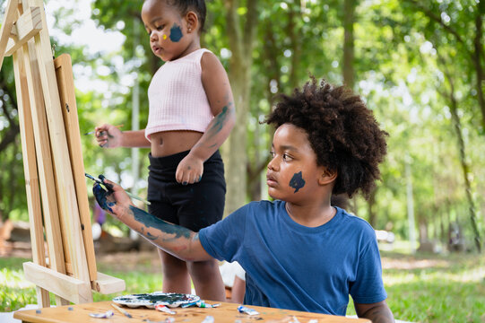 Portrait African American kid boy and girl painting in the park	