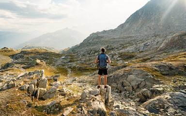Naklejka premium Hiker at the top of the pass with a backpack to enjoy a sunny day in the Alps. Mountain lake nearly fusing with the surrounding granite boulders, sediment gray Grimselsee lake.