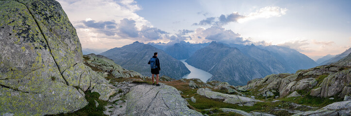 Fototapeta premium Panorama view of sediment gray Grimselsee lake in Switzerland. Amazing view on colorful clouds and layered mountains. Sunset or sunrise