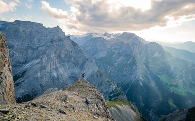 Man hiking accomplish success silhouette in mountains. Male hiker with arms outstretched on top of mountain looking peaks of Alps in Switzerland