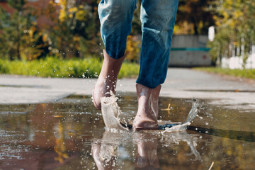 Woman wearing rain rubber boots walking running and jumping into puddle with water splash and drops in autumn rain.