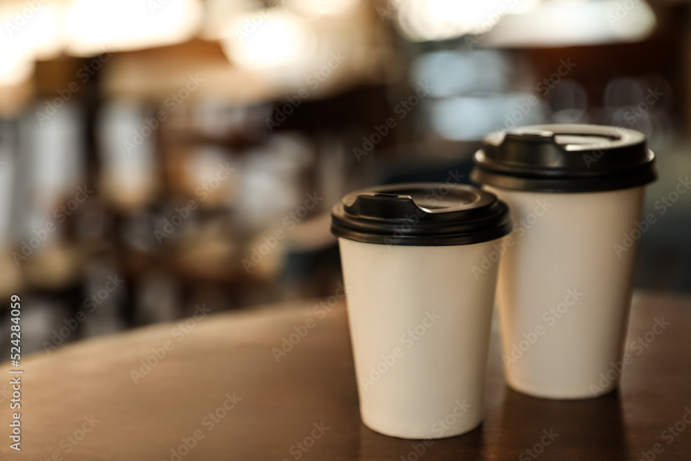 Poster Cardboard takeaway coffee cups with plastic lids on wooden table in outdoor cafe, space for text