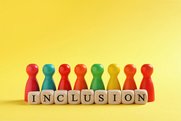 Colorful pawns and wooden cubes with word Inclusion on yellow background