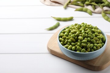 Bowl of delicious edamame beans on white wooden table, space for text