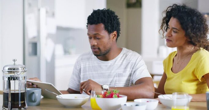 Happy, loving and caring couple kiss while eating breakfast at home on the weekend. Young african american attractive female enjoying a meal and bonding with her boyfriend at home in the kitchen