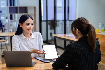 Two Asian businesswoman discuss investment project working and planning strategy with tablet laptop computer in modern office..