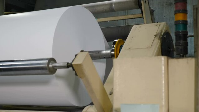 Paper production machine. Processing of secondary resources. Paper recycling. Paper being impregnated with formalin for furniture production. Moving roller with white paper. Roll unreeling for