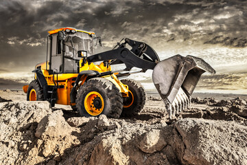 Powerful bulldozer or loader moves the earth at the construction site against the sky. An earthmoving machine is leveling the site. Construction heavy equipment for earthworks. - obrazy, fototapety, plakaty