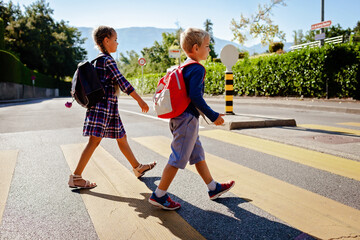 Pedestrian schoolchildren with backpacks crossing the road at a crosswalk on the way to school, back to school, school time, child safety, traffic road rules. Study and education concept, lifestyle