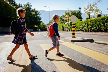 Young pedestrians with backpacks walk to school and cross the road at crosswalk, back to school,...