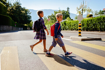 Boy and girl with backpacks walking to school and crossing the road at crosswalk, back to school, school time, child safety, young pedestrian road rules. Study and education concept, lifestyle